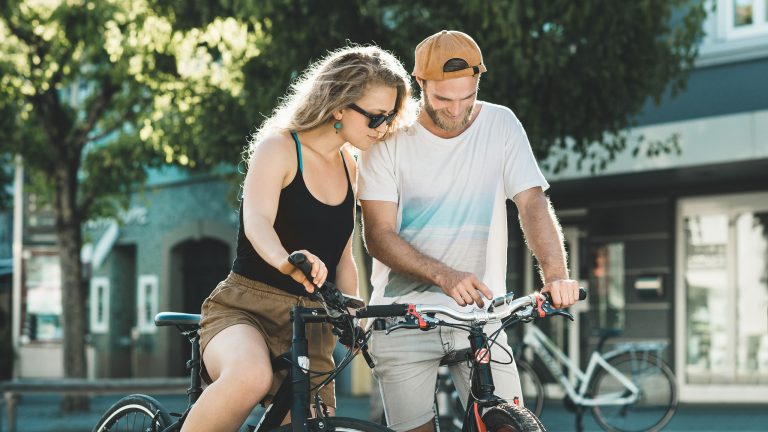 Gewusst wohin, Fahrrad-Routenplaner Zwei Personen auf Fahrrädern schauen auf ein Smartphone, das an einem der beiden Lenker befestigt ist.